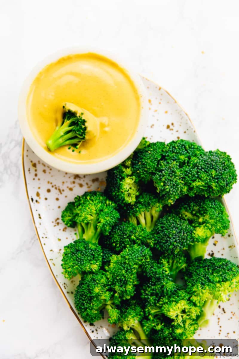 An inviting overhead shot showcasing perfectly cooked broccoli florets on a platter, with a small bowl of creamy vegan cheese sauce nestled beside it, a piece of broccoli resting in the sauce, ready for a healthy and delicious dip.