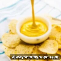 A stream of rich, creamy vegan cheese sauce beautifully drizzles into a bowl, centered on a plate surrounded by golden tortilla chips.