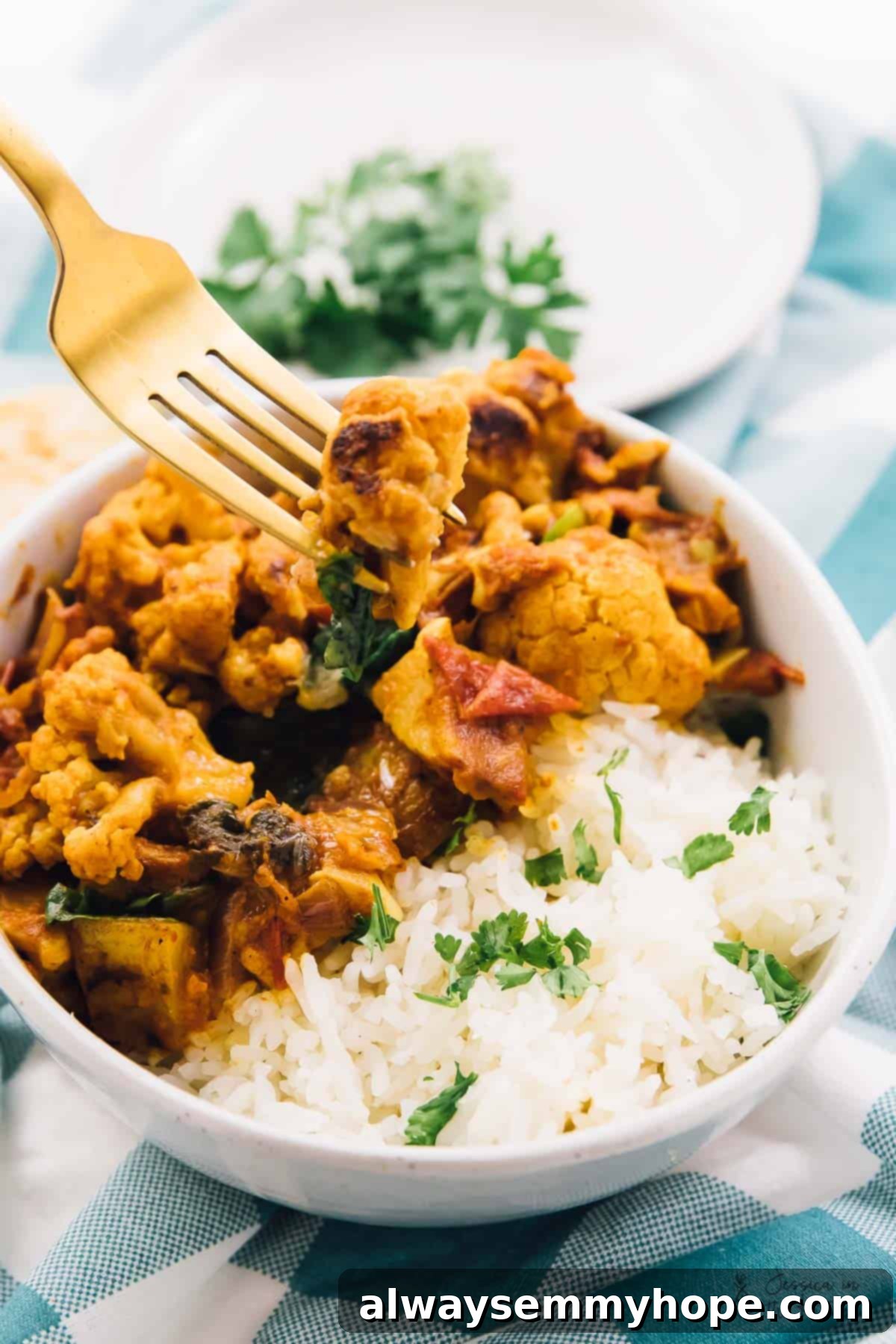 A gold fork digging into a bowl of cauliflower and potato curry.