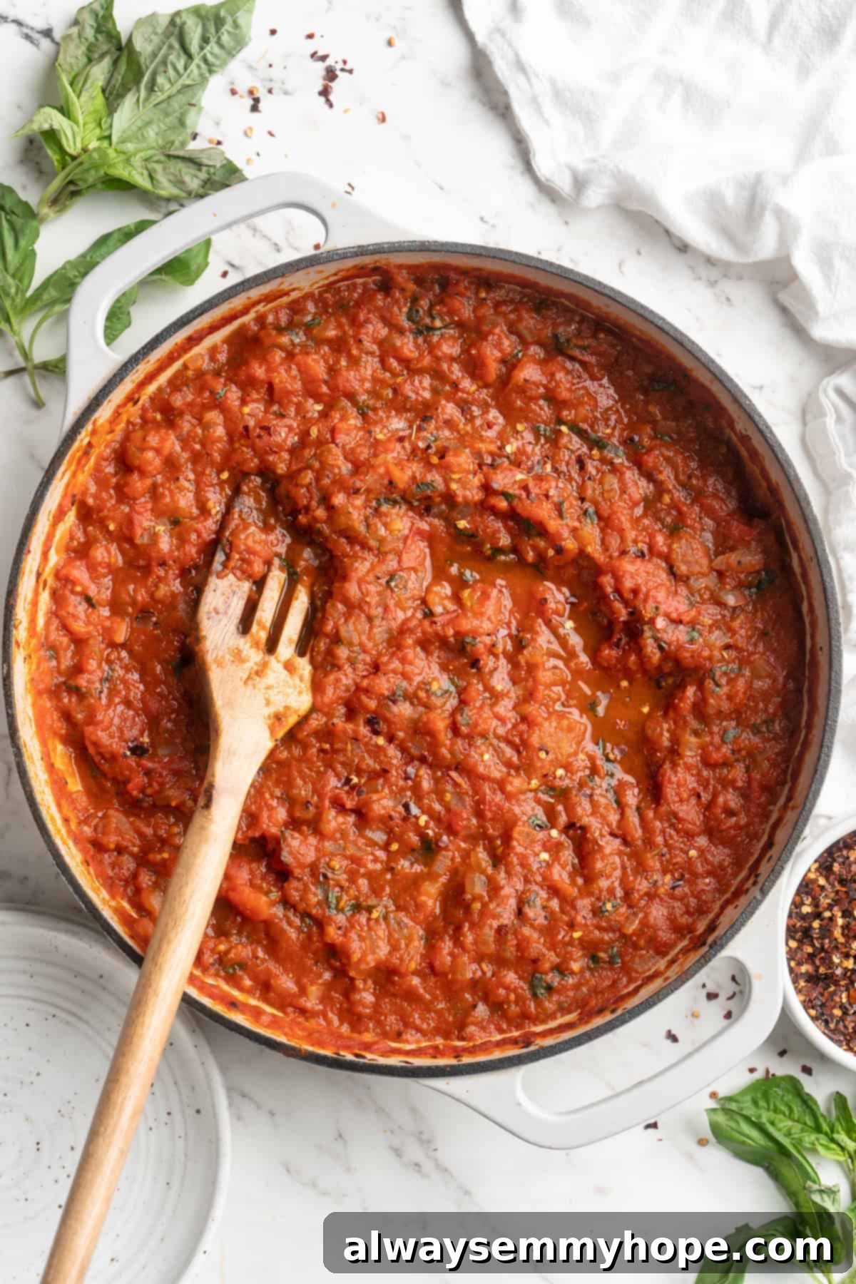 Overhead view of vibrant red arrabbiata sauce simmering in a skillet with a wooden spoon, ready to be served over pasta.