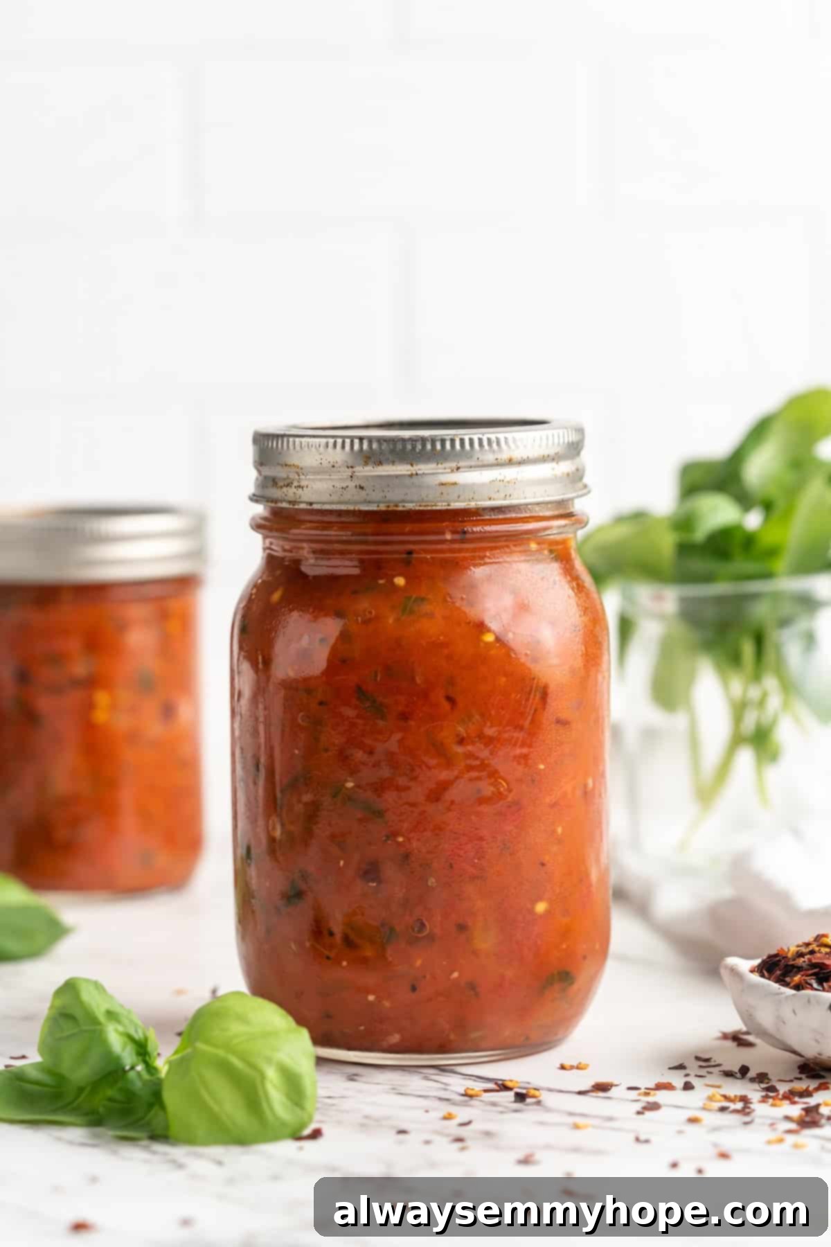 Three jars of homemade arrabbiata sauce, labeled and ready for storage or gifting, showcasing its rich red color.