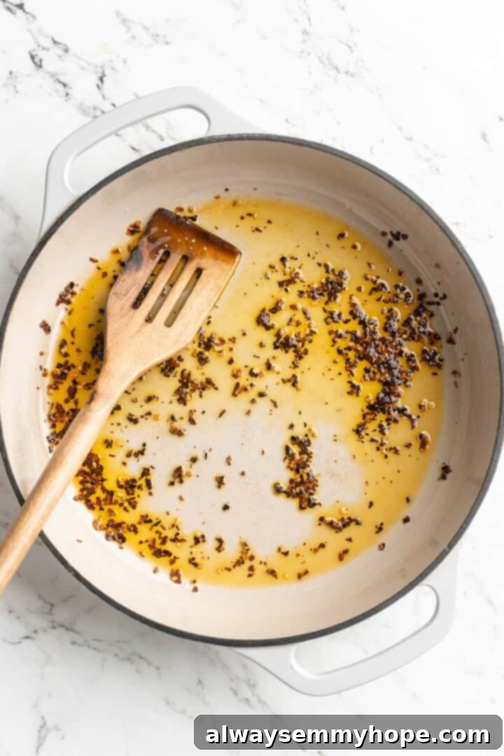 Close-up overhead view of red pepper flakes sizzling in hot olive oil in a skillet, infusing the oil with spicy flavor.