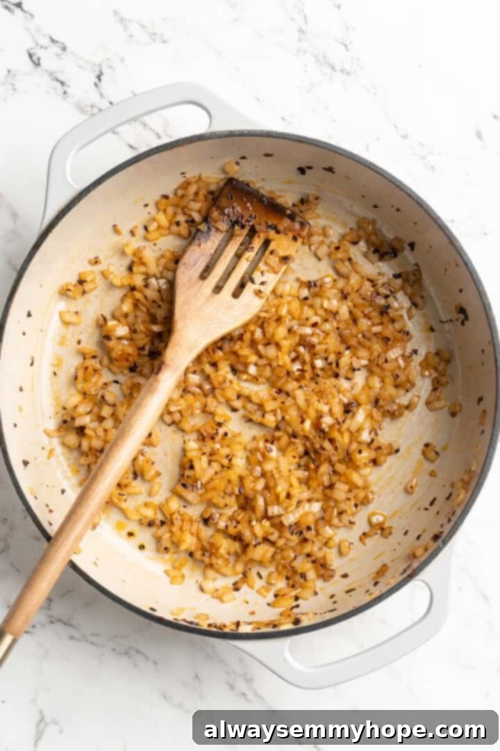 Overhead view of diced white onions softening in a skillet, turning translucent as they cook down.