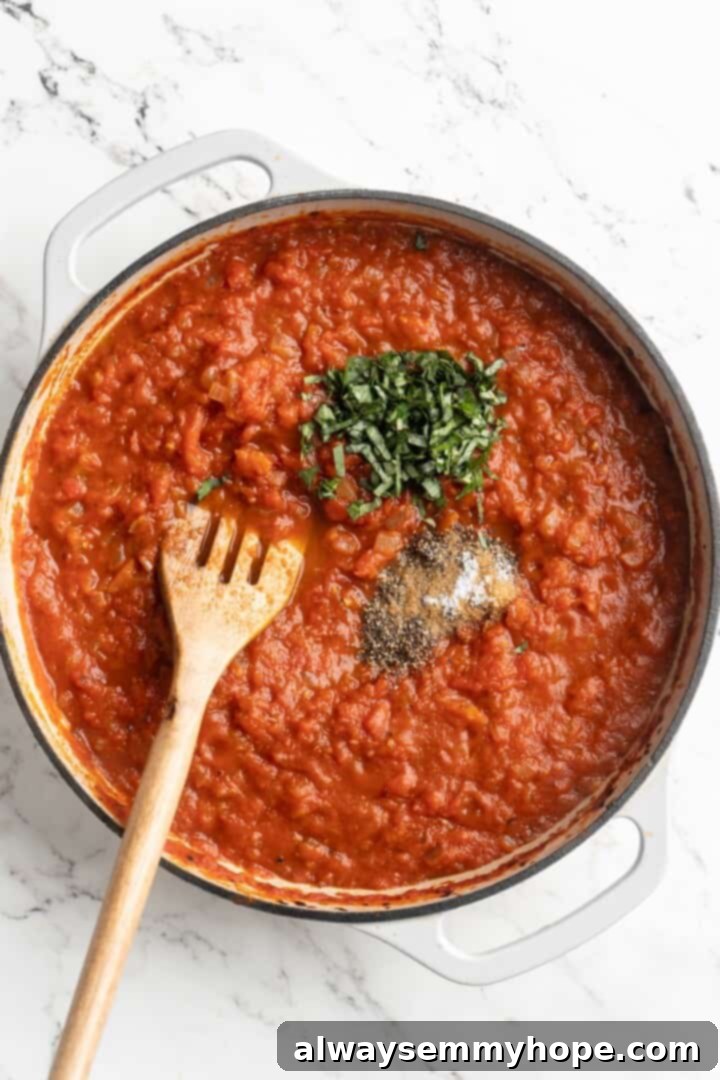 Overhead view of fresh basil leaves, sea salt, and black pepper being added to the simmering arrabbiata sauce in a skillet.