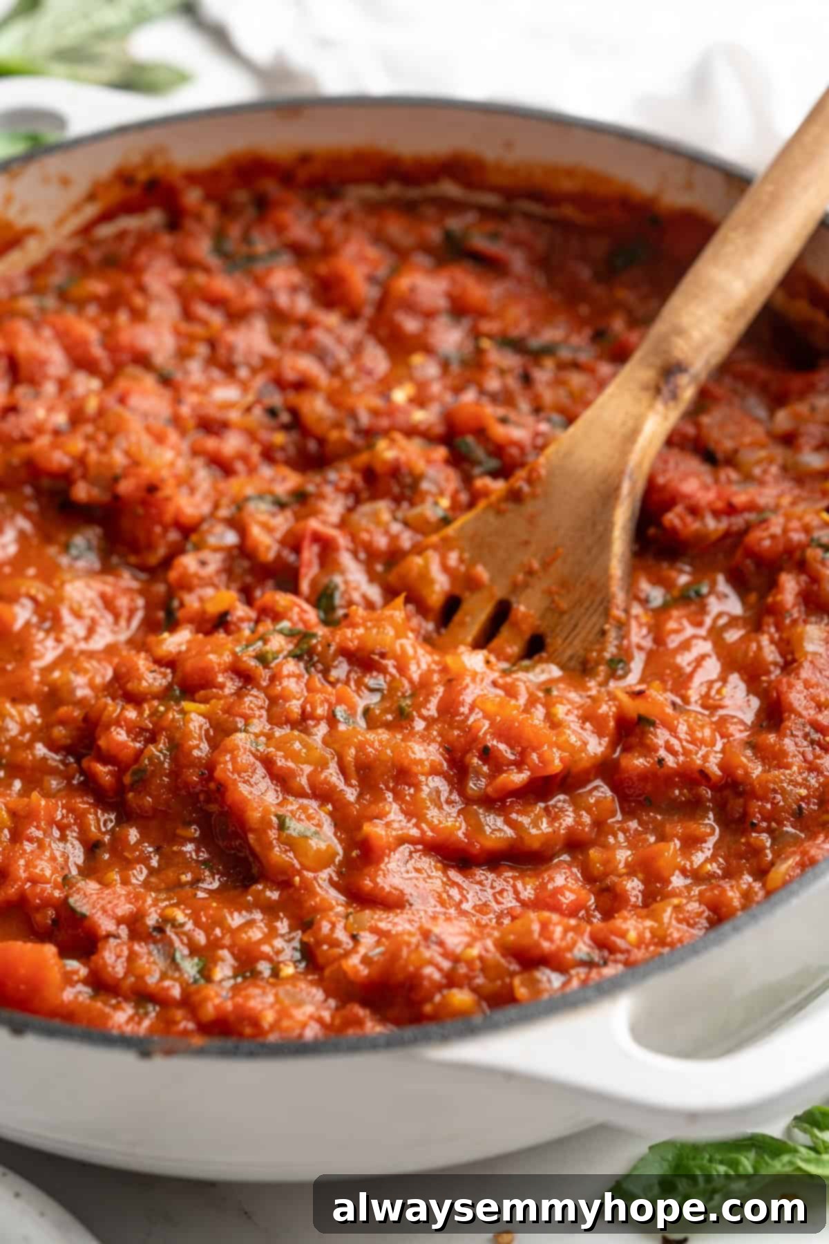 Arrabbiata sauce in a cast iron skillet with a wooden spoon, garnished with fresh basil, ready to be tossed with pasta.