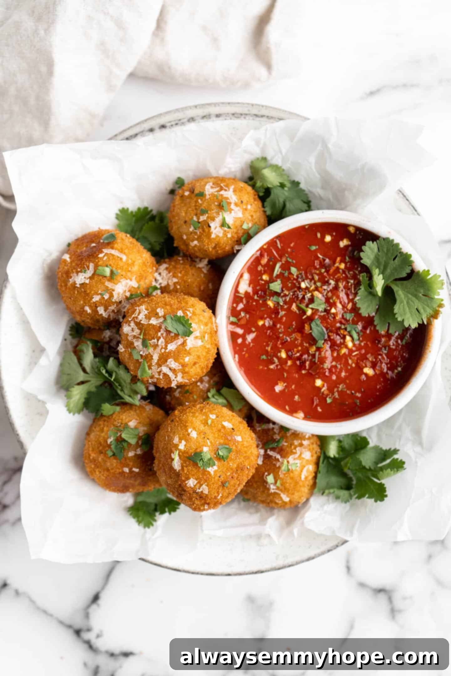 These vegan arancini are crispy, stuffed with melty mozzarella, and perfect for appetisers! Fry them the traditional way or use an air fryer! Vegan arancini in parchment-lined bowl with marinara sauce
