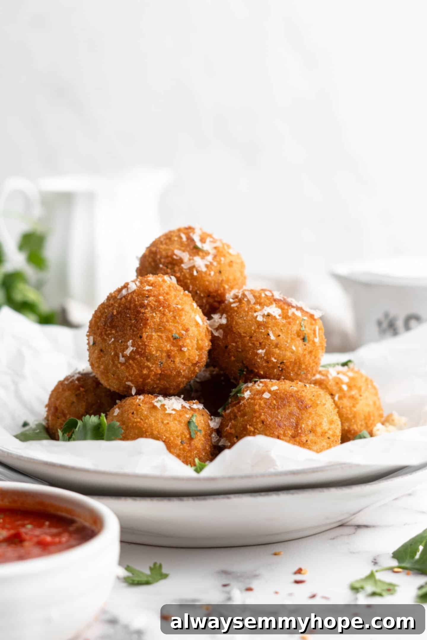 These vegan arancini are crispy, stuffed with melty mozzarella, and perfect for appetisers! Fry them the traditional way or use an air fryer! Pile of arancini on parchment-lined plate