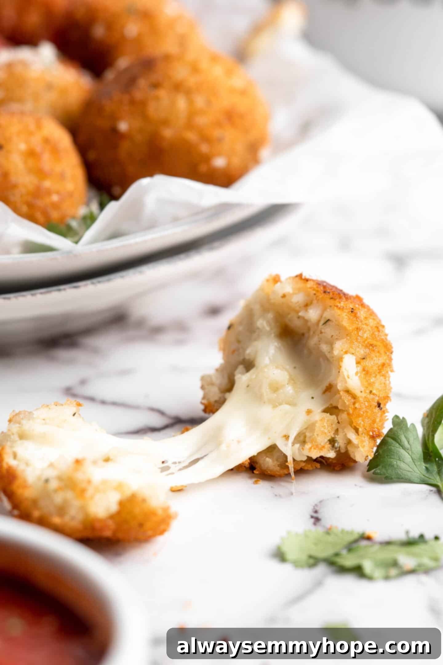 These vegan arancini are crispy, stuffed with melty mozzarella, and perfect for appetisers! Fry them the traditional way or use an air fryer! Two halves of an arancini, separated to show stretchy vegan cheese inside