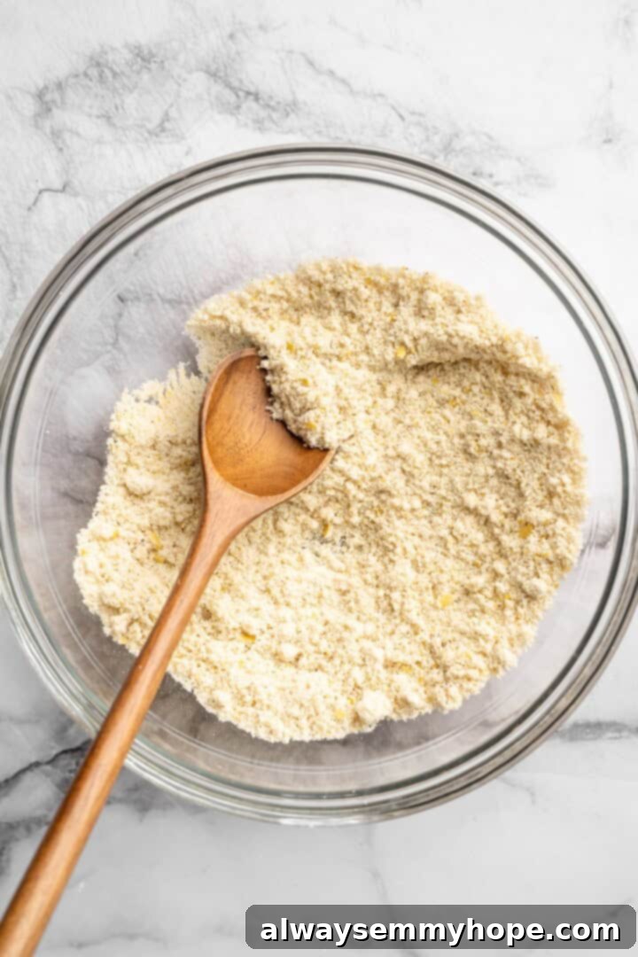 Stirring dry ingredients for almond flour pizza crust in a mixing bowl with a spoon.