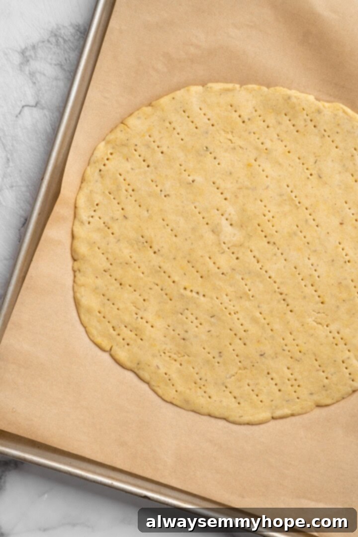 Overhead view of unbaked almond flour pizza crust on parchment-lined pan, pricked with a fork.