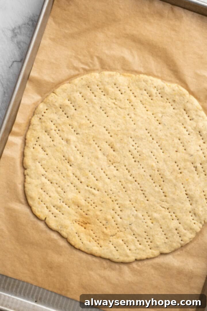 Overhead view of a par-baked almond flour pizza crust on a parchment-lined pan, golden and ready for toppings.