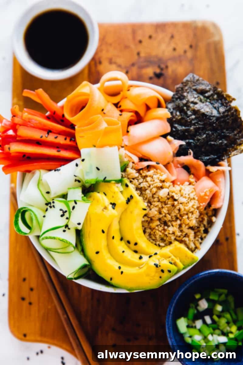 Top down shot of a vegan sushi rice bowl on a wooden board with sauce on the side.