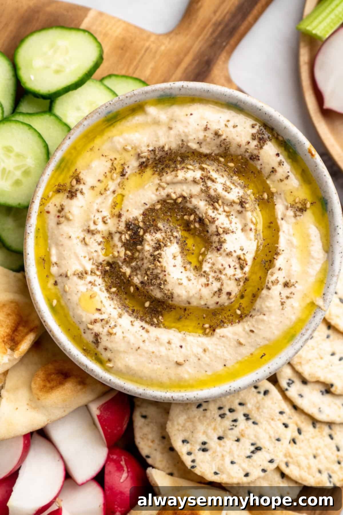 This easy Roasted Cauliflower Hummus gives the classic dip a low-carb makeover! I add roasted garlic too, which makes it extra delicious. Overhead view of a bowl of creamy roasted cauliflower hummus, elegantly garnished with a swirl of olive oil and a sprinkle of za'atar