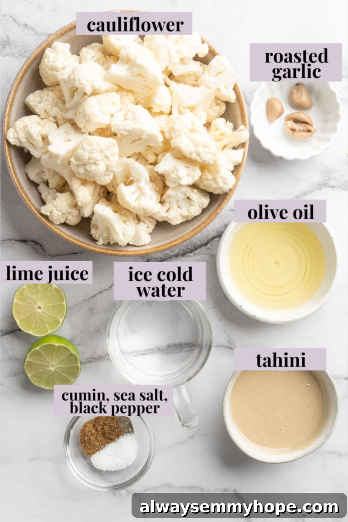 This easy Roasted Cauliflower Hummus gives the classic dip a low-carb makeover! I add roasted garlic too, which makes it extra delicious. Overhead view of fresh ingredients for roasted cauliflower hummus laid out neatly on a rustic wooden board, including cauliflower florets, olive oil, roasted garlic, tahini, lime, and seasonings