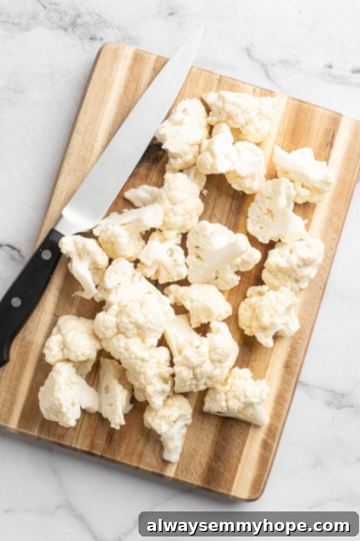 This easy Roasted Cauliflower Hummus gives the classic dip a low-carb makeover! I add roasted garlic too, which makes it extra delicious. Overhead view of cauliflower being cut into uniform florets on a wooden cutting board
