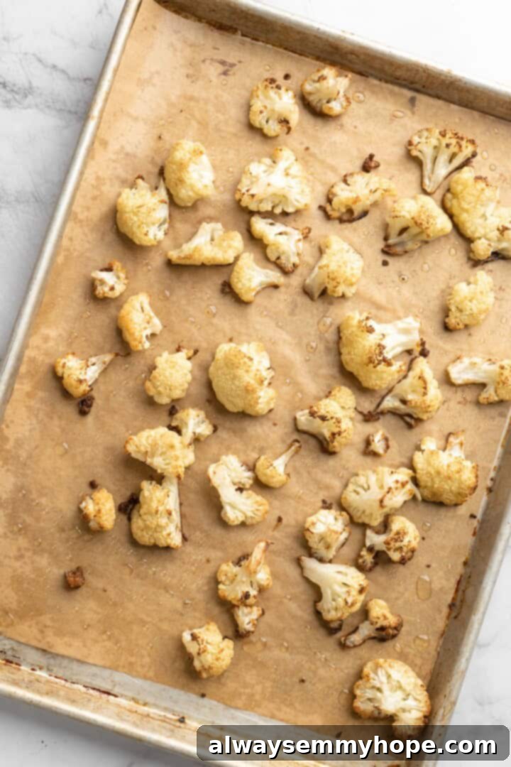This easy Roasted Cauliflower Hummus gives the classic dip a low-carb makeover! I add roasted garlic too, which makes it extra delicious. Overhead view of seasoned cauliflower florets spread evenly across a sheet pan, ready to be roasted to golden perfection
