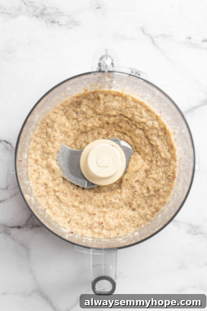 This easy Roasted Cauliflower Hummus gives the classic dip a low-carb makeover! I add roasted garlic too, which makes it extra delicious. Overhead view of roasted cauliflower, olive oil, roasted garlic, and seasonings placed in a food processor, ready for blending