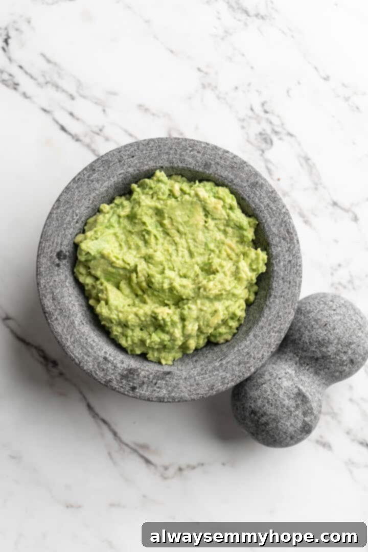 This easy guacamole recipe is the ultimate crowd pleaser! It’s incredibly fresh and flavourful, and it takes just 15 minutes to make. Overhead view of perfectly mashed avocado in a traditional molcajete, ready for additional ingredients