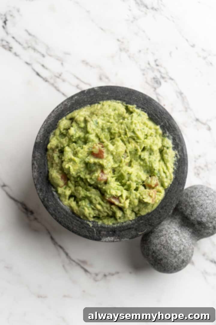 This easy guacamole recipe is the ultimate crowd pleaser! It’s incredibly fresh and flavourful, and it takes just 15 minutes to make. Overhead view of freshly prepared guacamole in a molcajete, garnished and ready to serve