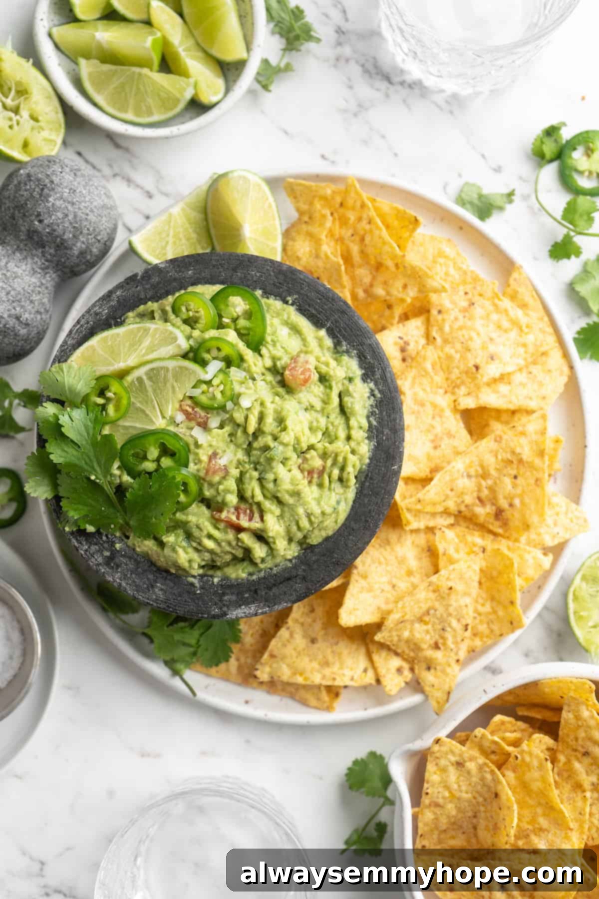 This easy guacamole recipe is the ultimate crowd pleaser! It’s incredibly fresh and flavourful, and it takes just 15 minutes to make. Overhead view of fresh homemade guacamole in a bowl, served with crisp tortilla chips on a large white plate