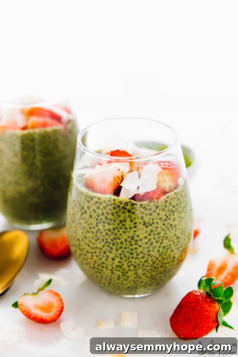 Two glasses of vibrant green matcha chia pudding, beautifully topped with fresh strawberries and delicate coconut flakes, set against a bright background.