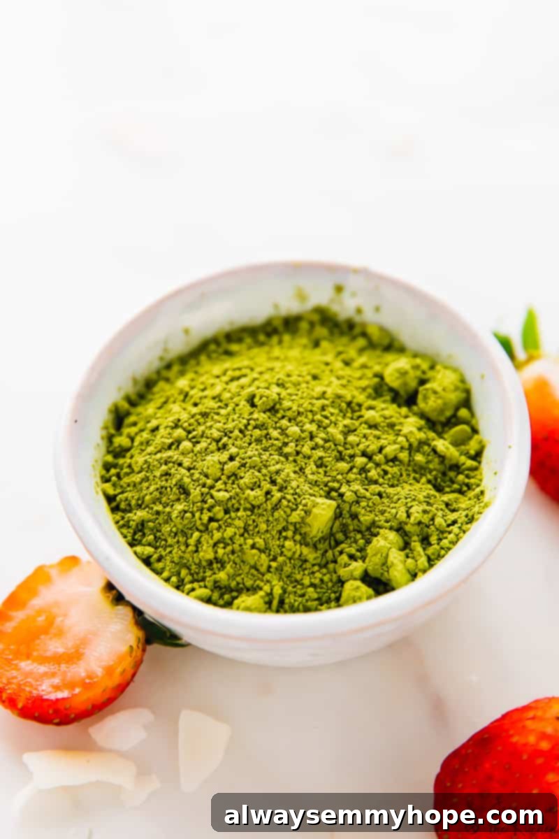 Bright green matcha green tea powder in a delicate white bowl, surrounded by fresh red strawberries, suggesting ingredients for a healthy recipe.