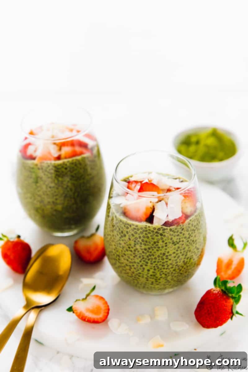 Two vibrant matcha green tea chia puddings arranged on a white marble cutting board, generously garnished with fresh chopped strawberries and large, flaky coconut pieces, ready for a healthy meal.
