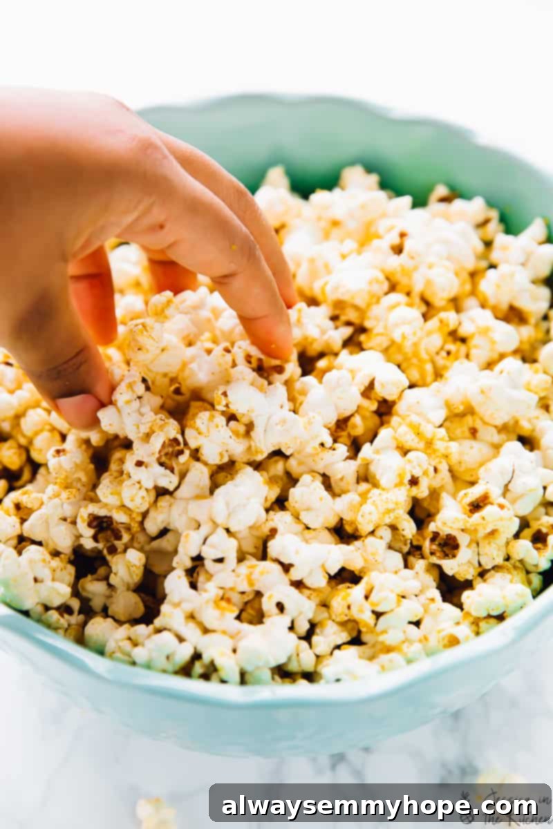 A hand grabbing a handful of freshly popped and seasoned cheesy vegan popcorn from a bowl.