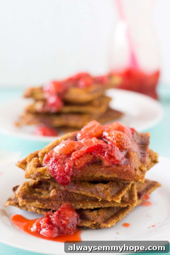 A stack of peanut butter waffles lavishly covered in a sweet strawberry compote, ready to be devoured.