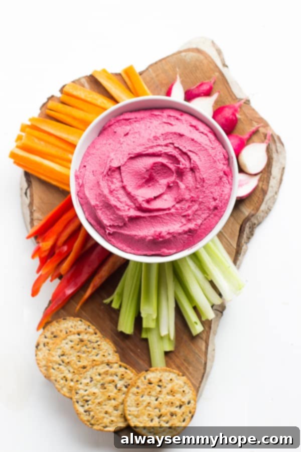 Overhead shot of beet hummus, with vegetables and crackers around it. 