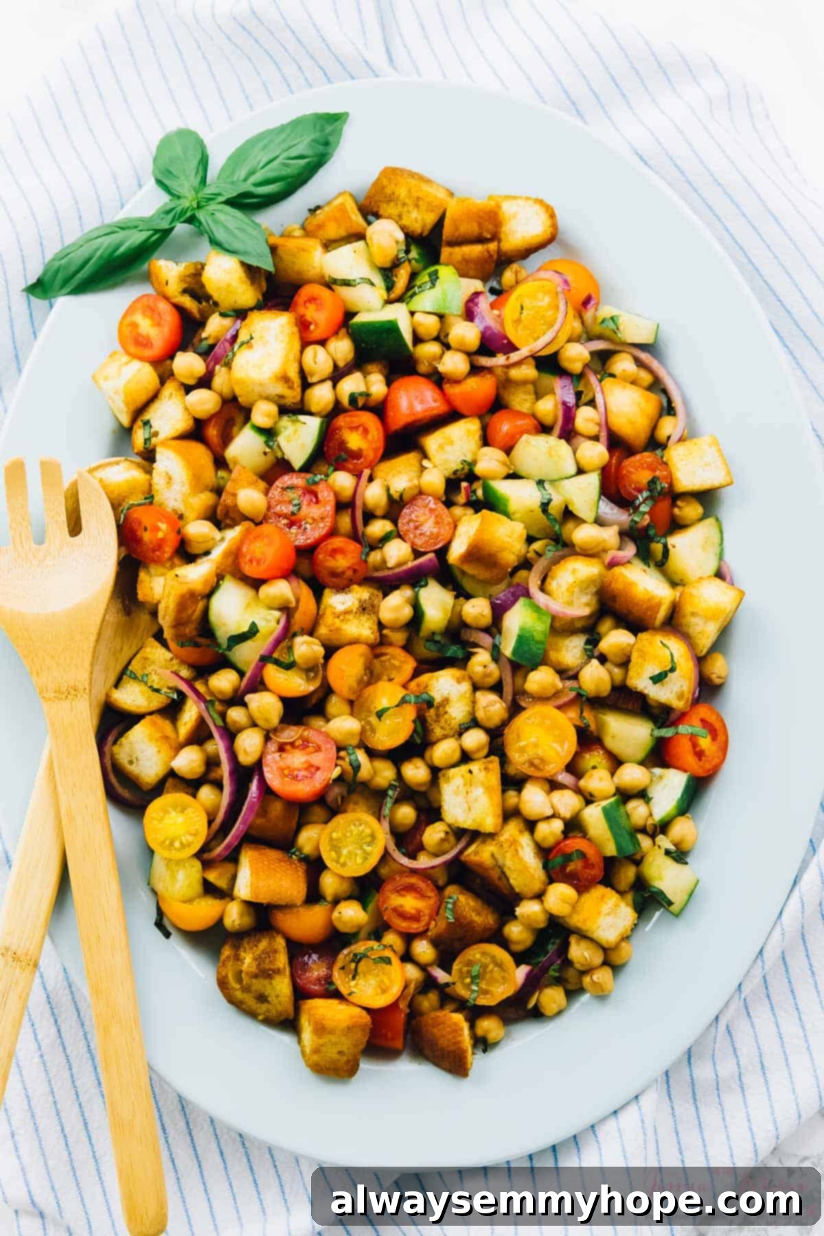 Top down view of chickpea panzanella salad on a long plate with a salad fork on the side.