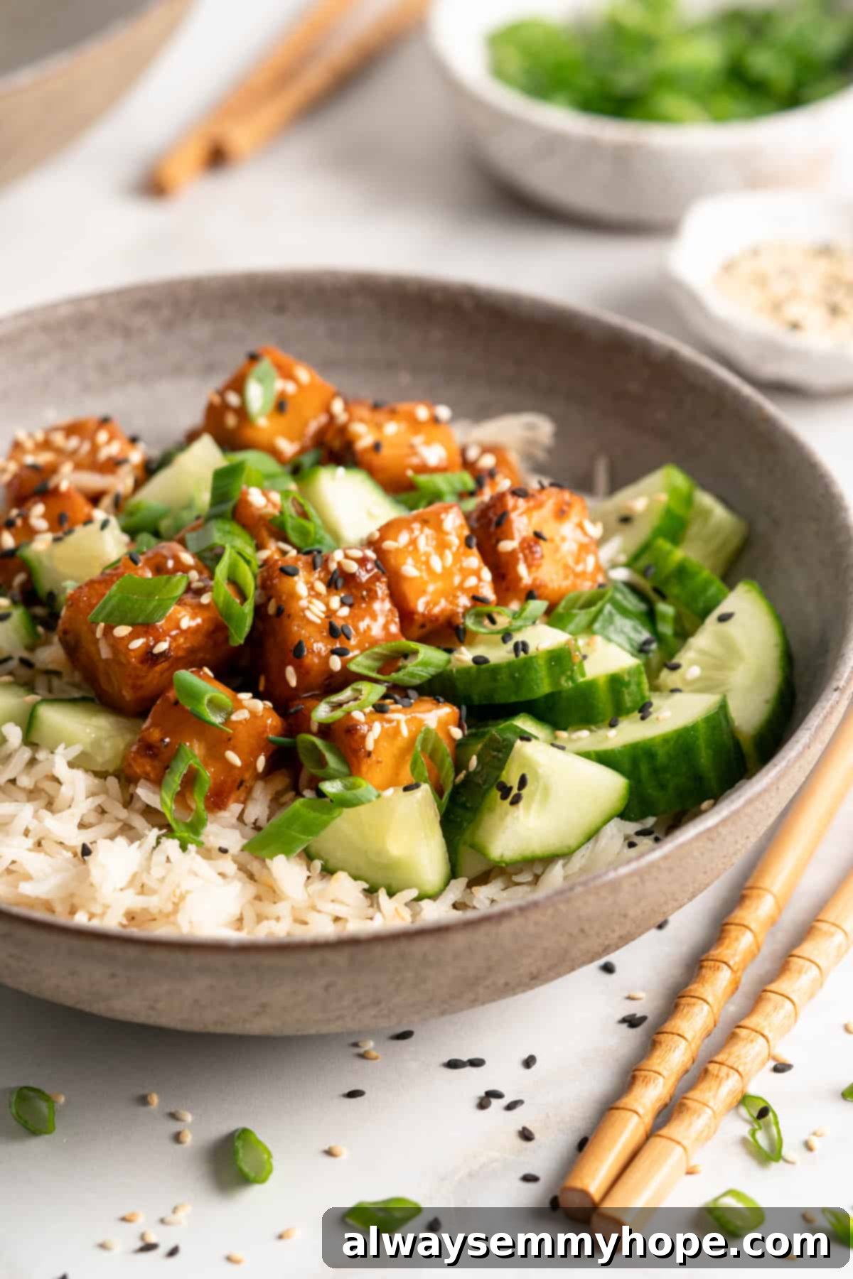 A vibrant bowl filled with fluffy white rice, fresh cucumber slices, and golden-brown air fryer orange tofu, garnished with sesame seeds.