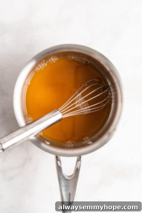 Orange sauce simmering in a saucepan with a whisk, showing the initial stage of sauce preparation.