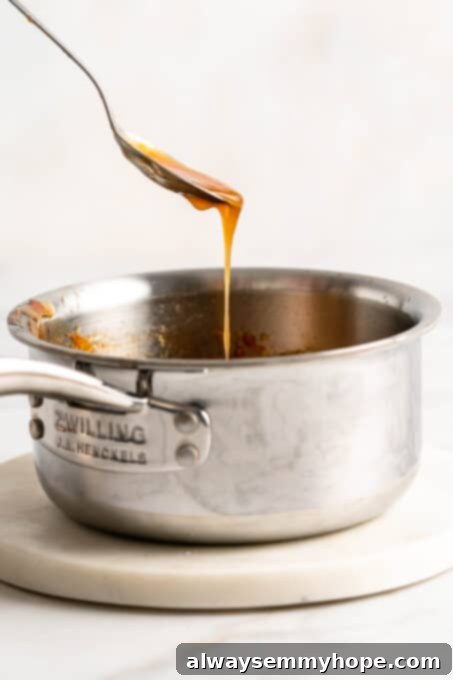 A spoonful of thick, glossy orange sauce dripping back into the saucepan, indicating it has reached the perfect consistency.