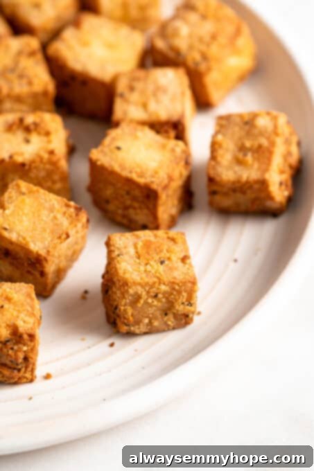 A close-up view of golden-brown, crispy air-fried tofu pieces in the air fryer basket, showcasing their perfect texture after cooking.