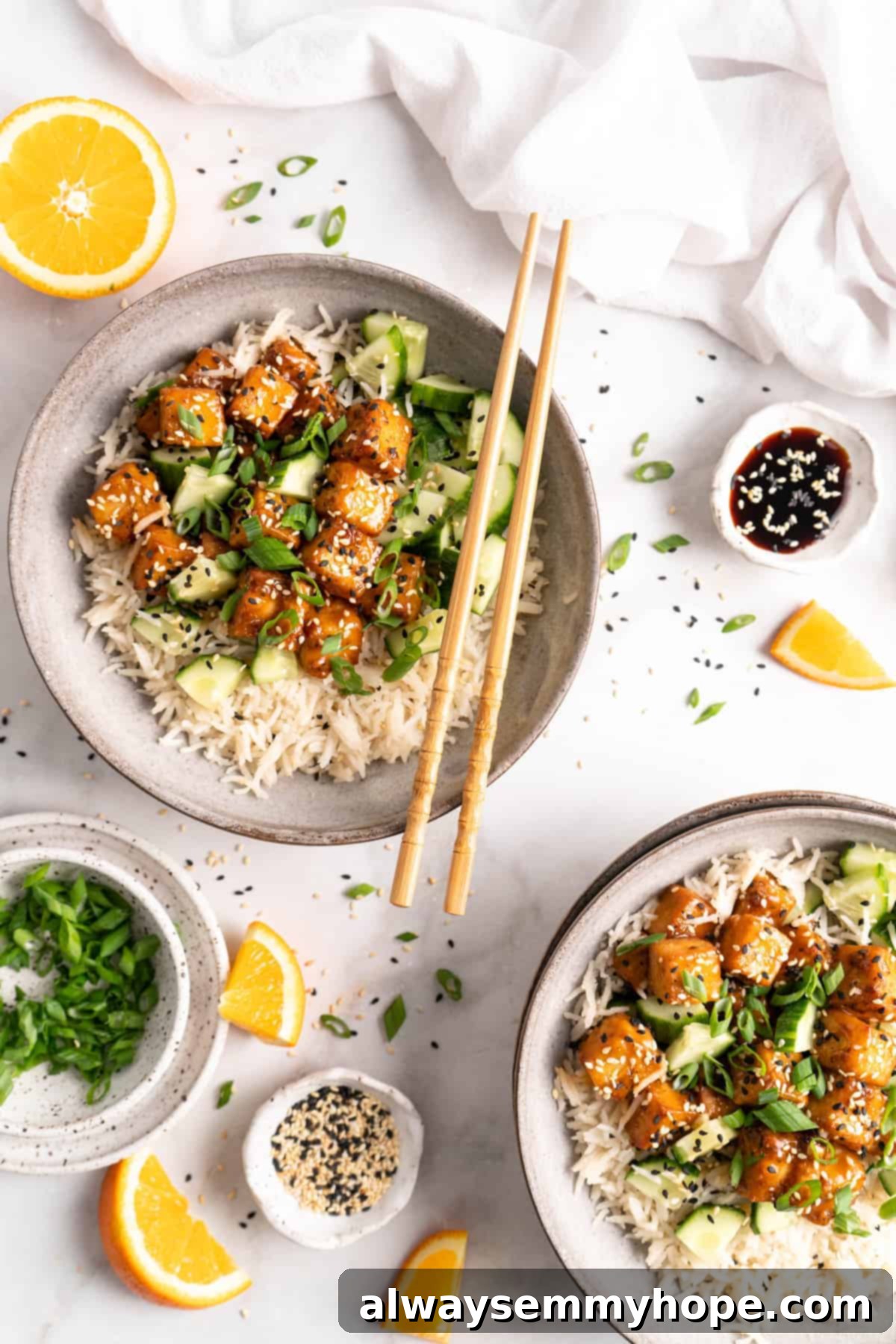 Two bowls of air fryer orange tofu served with rice and fresh cucumber, garnished with sesame seeds, ready to eat.