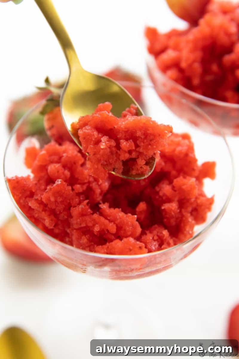 Strawberry granita in a spoon hovering over the glass, showcasing its icy, refreshing texture.