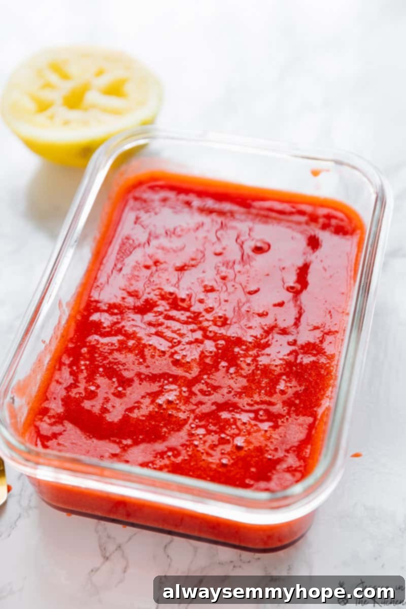 Liquid version of strawberry granita mixture (before freezing) with a lemon half in the background, hinting at its fresh ingredients.
