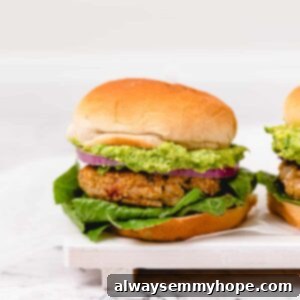 Two golden brown veggie burgers with avocado, red onion, and lettuce on fluffy vegan buns