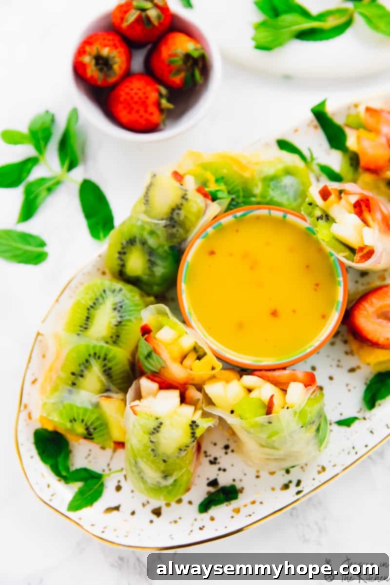 Tropical Fruit Spring Rolls with Sunshine Mango Dip 2 A vibrant platter showcasing an assortment of fresh summer fruits like mango, kiwi, strawberries, and apples, beautifully wrapped in translucent rice paper to create Summer Fruit Spring Rolls. Some rolls are cut in half to reveal the colorful fruit filling, arranged alongside a small bowl of creamy mango dipping sauce. This colorful, crunchy, vegan, and gluten-free meal is perfect for any occasion.