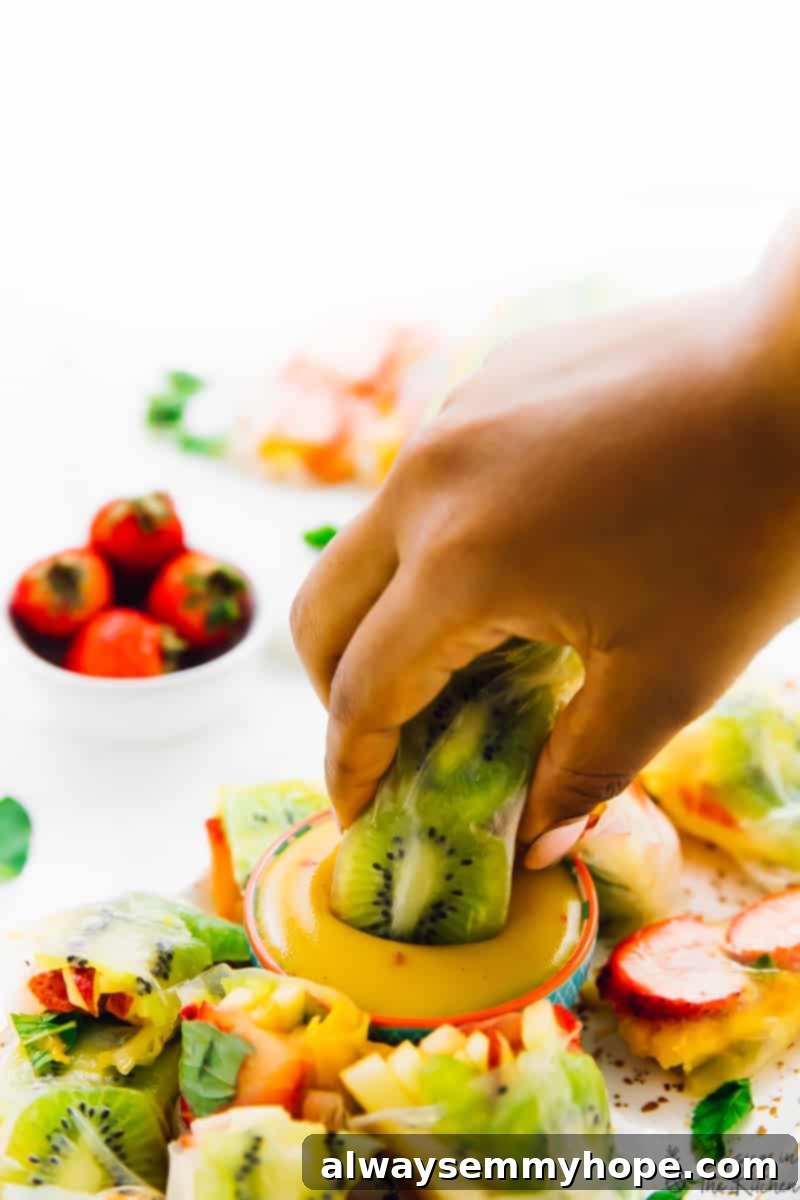 Tropical Fruit Spring Rolls with Sunshine Mango Dip 4 A close-up shot of a hand dipping a vibrant Summer Fruit Spring Roll into a small white bowl filled with creamy mango dipping sauce. The translucent rice paper of the roll reveals colorful fruit slices within, emphasizing the freshness and appeal of the dish, perfectly highlighting the delicious combination of fresh fruit and the sweet, tangy dip.