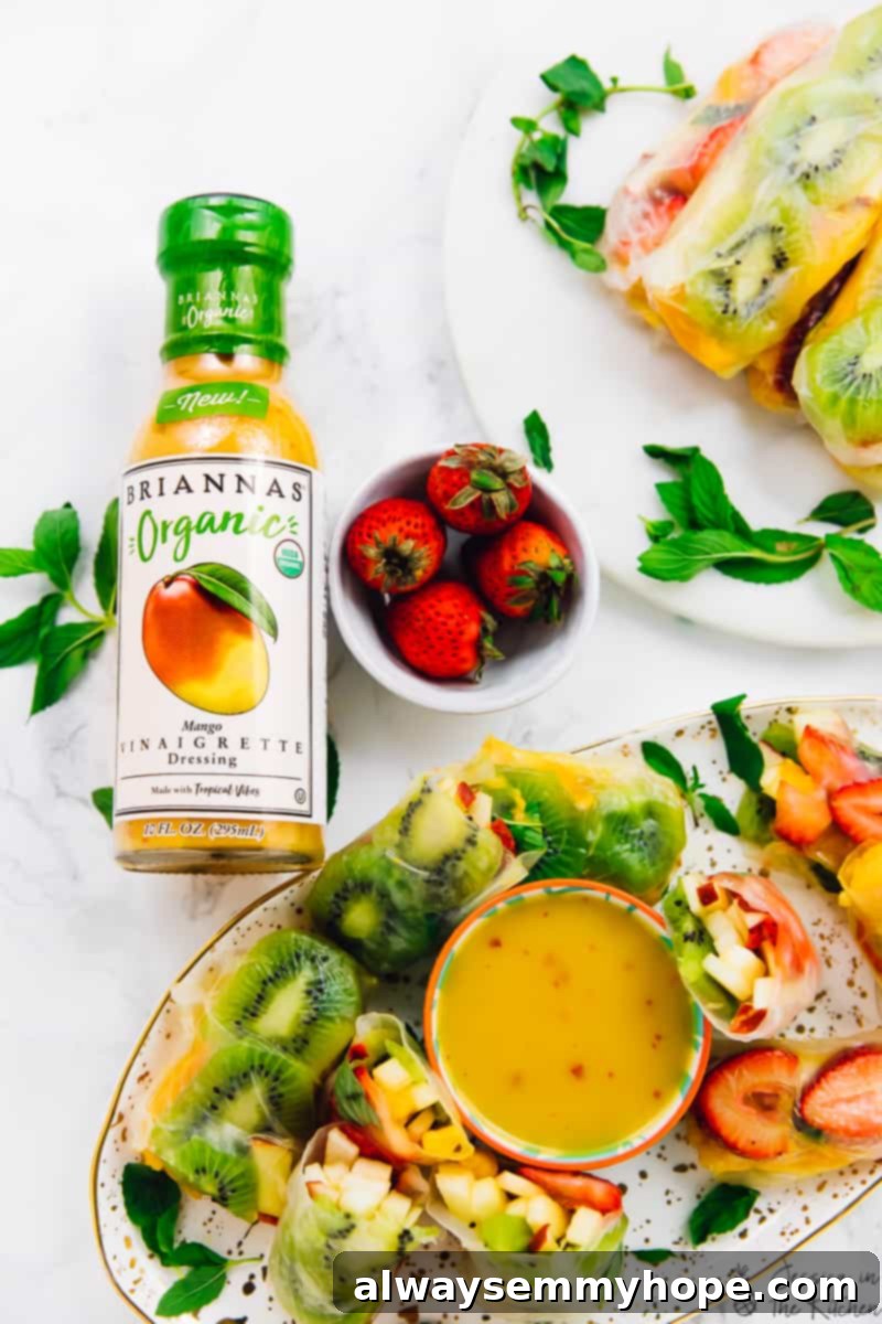 Tropical Fruit Spring Rolls with Sunshine Mango Dip 5 A top-down shot presenting multiple platters laden with beautifully arranged Summer Fruit Spring Rolls, some whole and some cut in half to showcase their colorful interiors. A bottle of BRIANNAS Organic Mango Vinaigrette stands prominently nearby, emphasizing the perfect pairing for these refreshing, healthy, and delicious vegan and gluten-free treats.