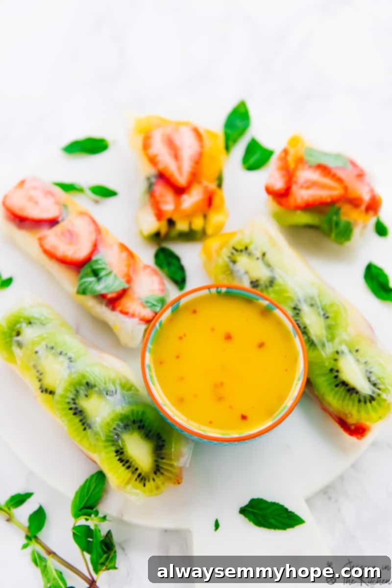 Tropical Fruit Spring Rolls with Sunshine Mango Dip 6 A beautifully presented plate of colorful Summer Fruit Spring Rolls, with some rolls sliced in half to reveal the vibrant layers of mango, kiwi, strawberries, and apple. A small bowl of mango dipping sauce accompanies the rolls, highlighting this fresh, healthy, vegan, and gluten-free appetizer or dessert.