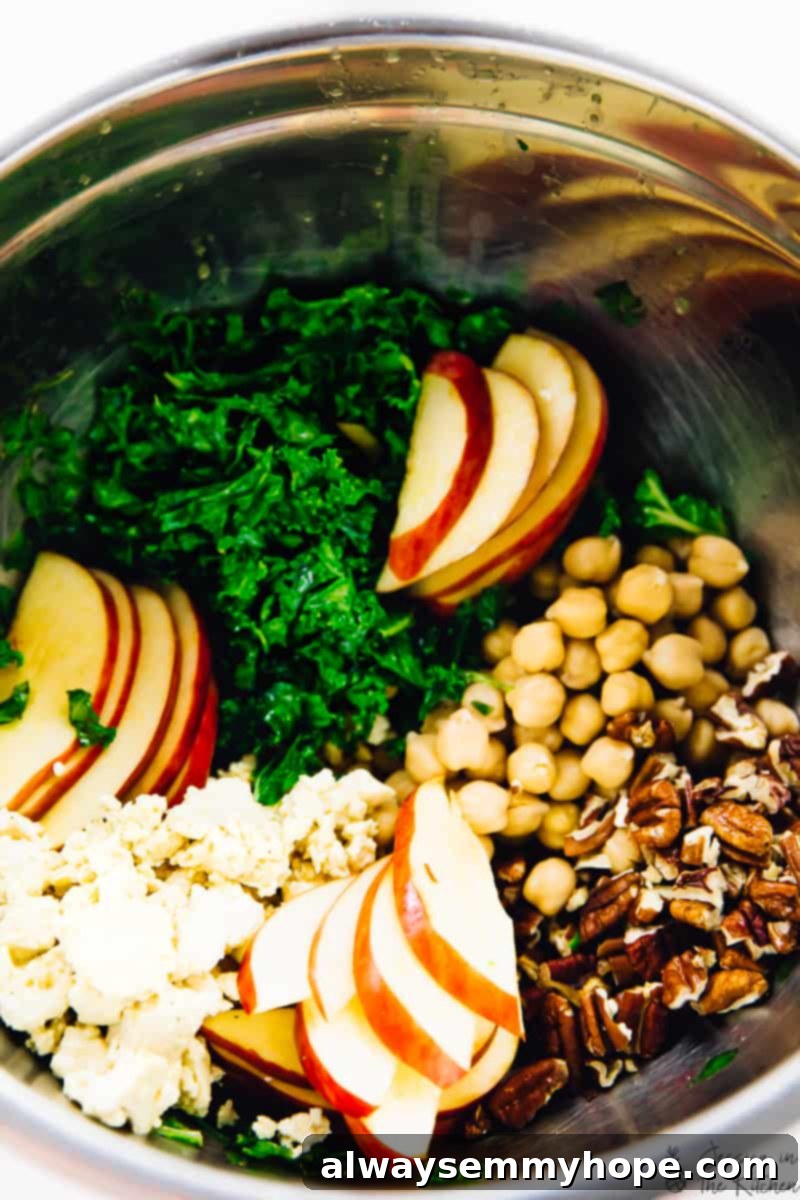 All the vibrant ingredients for the kale apple salad, including chopped kale, sliced apples, chickpeas, and toasted pecans, combined in a large metal mixing bowl, ready to be tossed.