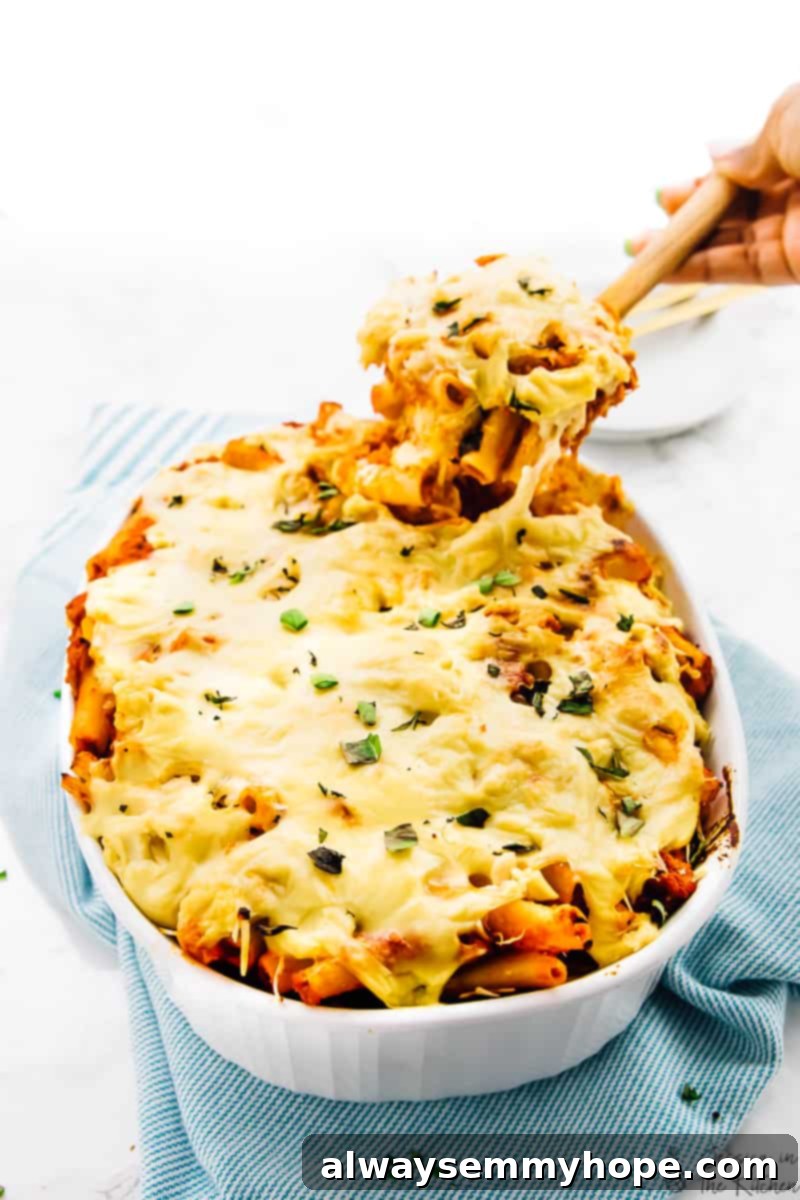 Photo of a vegan cheese baked pasta being pulled out of the serving dish with a cheese pull, highlighting its gooey texture.
