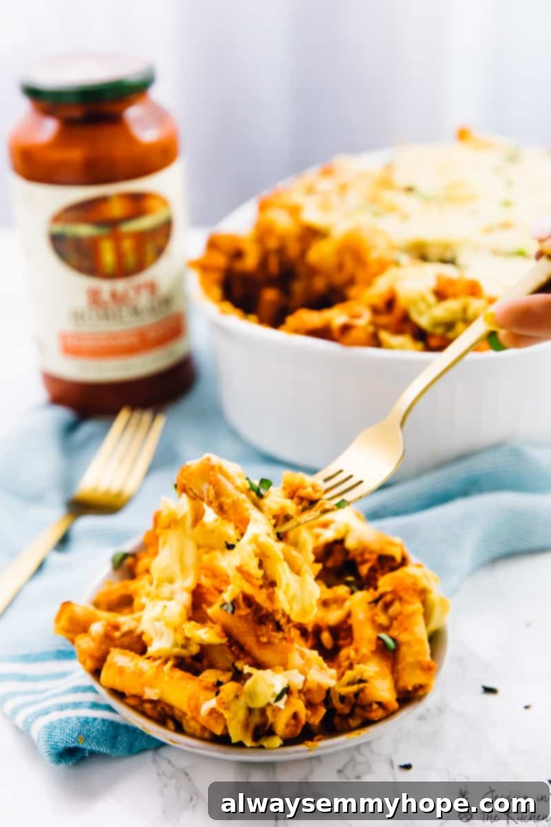 A fork digging into a bowl of baked ziti, showing off the melted cheese and rich sauce.