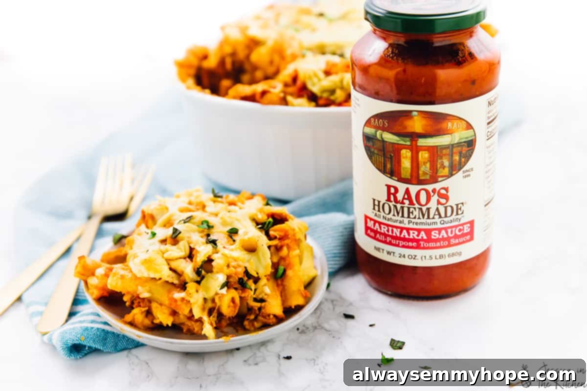 Cheesy baked ziti in a baking dish with a jar of Rao's Homemade marinara sauce beside it, showcasing the key ingredient.
