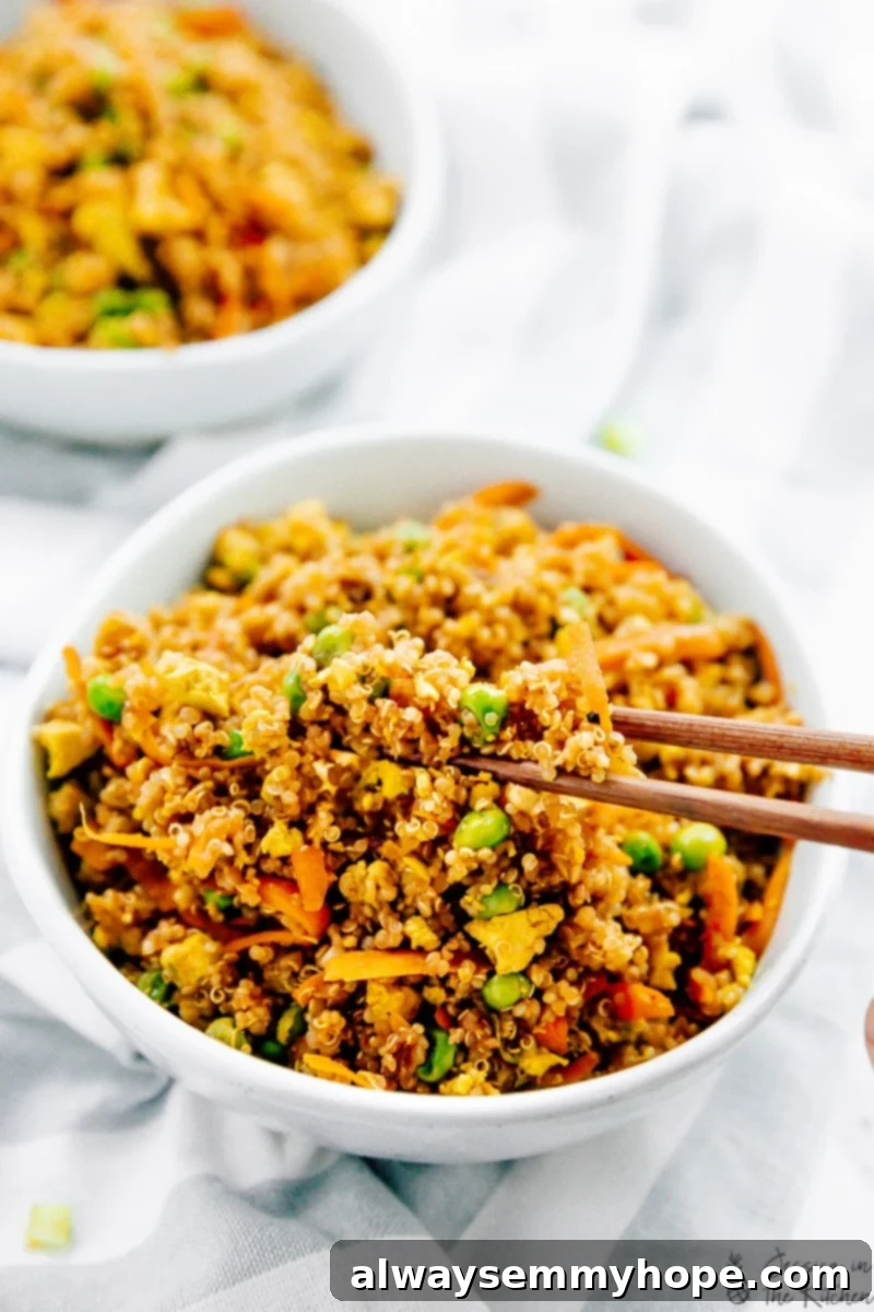 Chopsticks picking up a flavorful bite of vegan quinoa fried rice from a white bowl