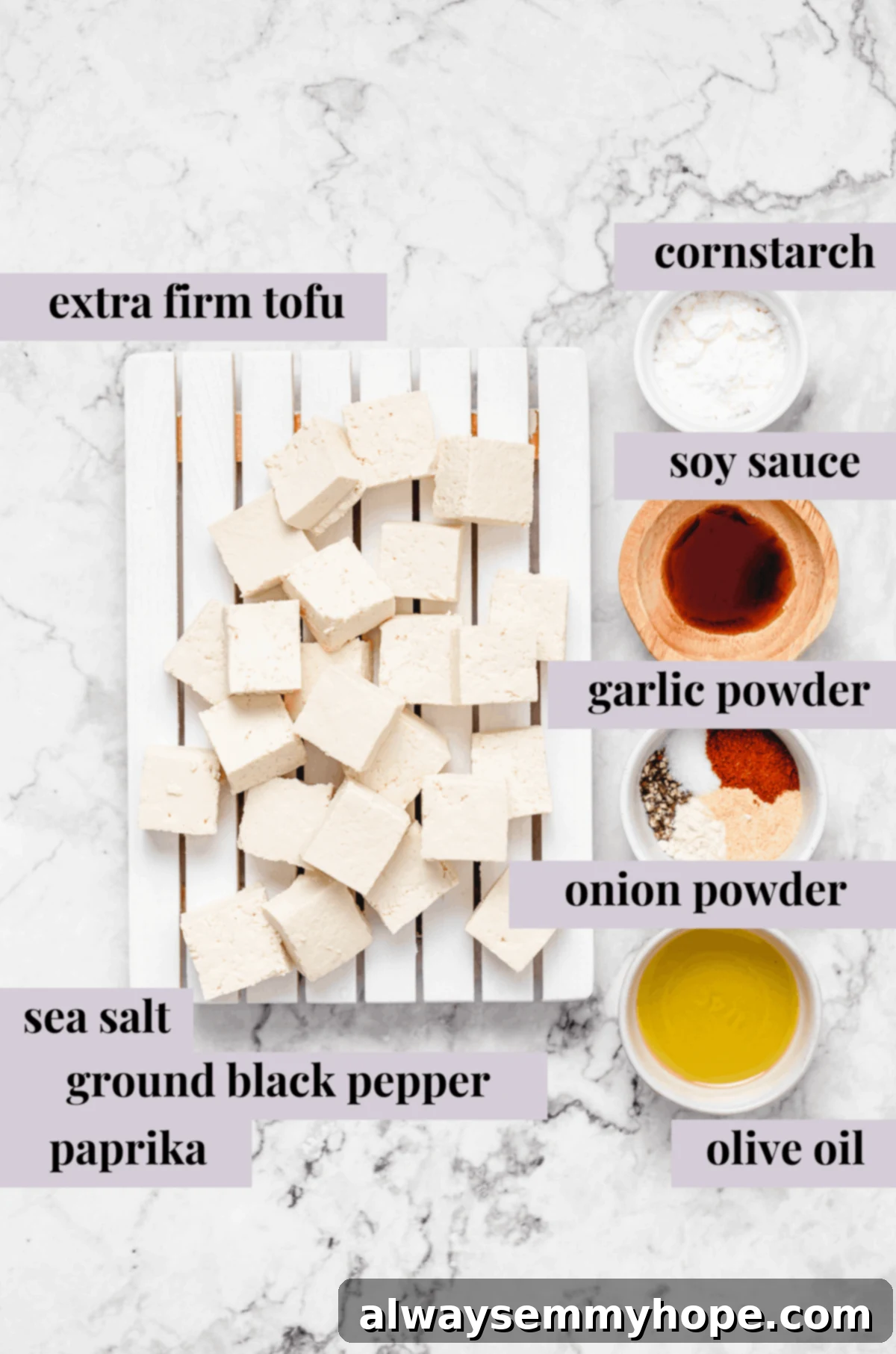 Essential ingredients laid out for making the best crispy baked tofu: extra-firm tofu, cornstarch, soy sauce, oil, and seasonings. Cubed extra-firm tofu on a white cutting board, surrounded by bowls of cornstarch, soy sauce, a mix of seasonings, and olive oil, prepped for marination.