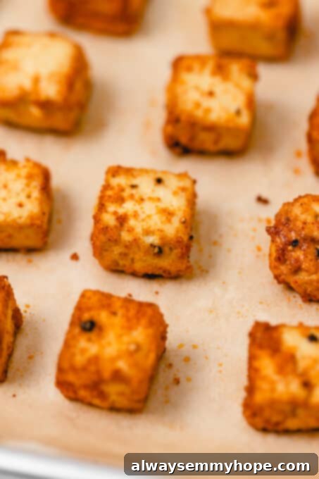 Freshly baked crispy tofu, ready to be served, showcasing its golden-brown exterior. Perfectly baked, golden-brown tofu cubes on a baking sheet with parchment paper, dusted with visible seasonings.
